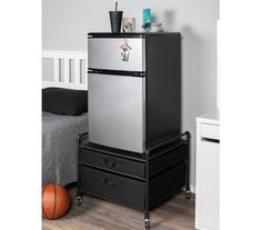 a black and silver refrigerator sitting on top of two drawers in a bedroom next to a bed