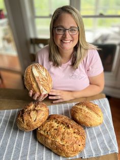 a woman sitting at a table with three loaves of bread