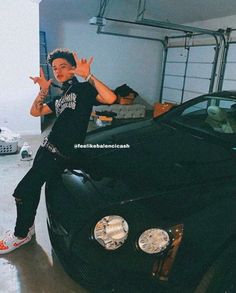 a man sitting on the hood of a black sports car in front of a garage