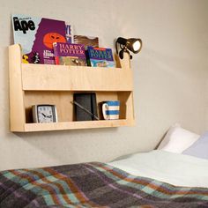 a bed with a wooden shelf on the wall above it that is filled with books