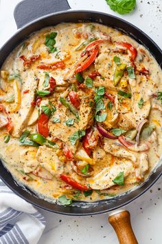 a pan filled with chicken and vegetables on top of a white table next to a wooden spoon