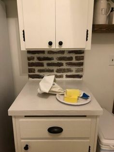 a kitchen with white cabinets and a counter top that has a plate on it, next to a toilet