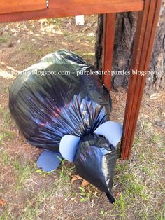 a black trash bag sitting on the ground next to a wooden table with a blue ribbon wrapped around it