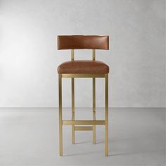 a gold bar stool with a brown leather seat and backrest in front of a white wall