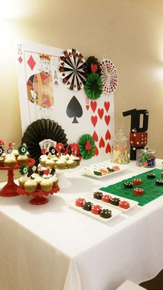 a table topped with cakes and cupcakes next to a casino card wall decoration