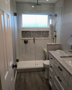 a bathroom with a walk in shower next to a white toilet and sink under a window