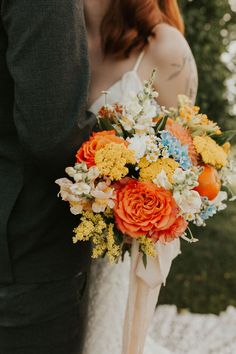 a bride and groom standing next to each other in front of trees with an orange bouquet