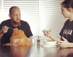 two people sitting at a table eating noodles