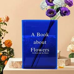 a book about flowers is sitting on a table with some flowers in the vase next to it