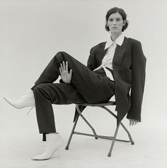 a woman sitting in a chair with her hand on her hip and wearing white shoes