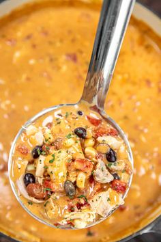 a ladle full of soup with chicken, beans and cheese in it is being held by a spoon