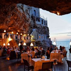 people are sitting at tables in front of an ocean view restaurant on the cliff side