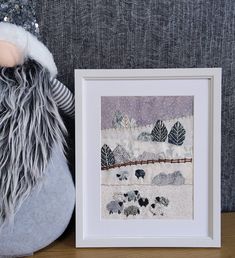 a stuffed animal sitting next to a framed art print on a table with a snow covered wall behind it