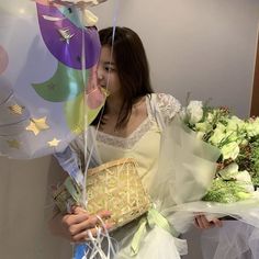 a woman holding flowers and balloons in her hands