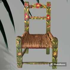 a chair made out of wicker and painted with flowers on the back, sitting in front of a palm tree