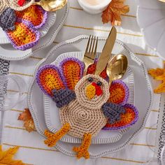 a crocheted turkey sitting on top of a plate next to a fork and knife