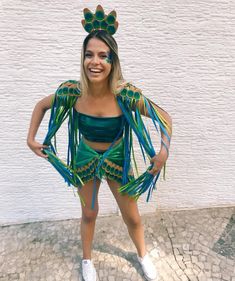 a woman wearing a green and blue costume with feathers on her head standing in front of a white wall