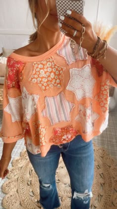 a woman taking a selfie with her cell phone while wearing ripped jeans and an orange top