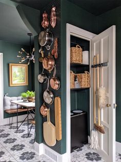 a kitchen with green walls and white cupboards filled with utensils hanging on the wall