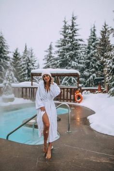 a woman in a bathrobe standing next to a swimming pool with snow on the ground