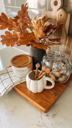 a wooden tray topped with coffee cups next to a vase filled with leaves and cinnamon sticks