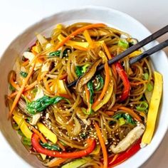 a white bowl filled with noodles and vegetables next to chopsticks on a table