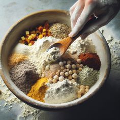 a bowl filled with different types of spices and seasonings next to a hand holding a wooden spoon