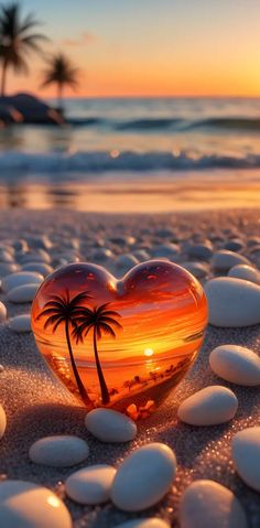 a heart shaped glass piece sitting on top of a sandy beach next to the ocean