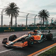 an orange and blue race car driving down the track with palm trees in the background