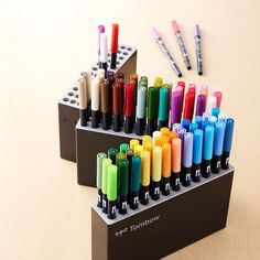 several pens are lined up in a holder on the table next to markers and pencils