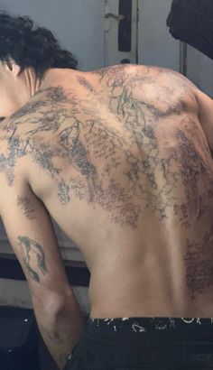 a man with tattoos on his back standing in front of a mirror