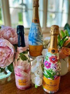 three bottles of champagne sitting on top of a wooden table next to pink flowers and peonies