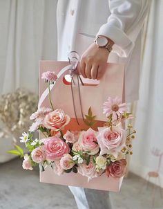 a person holding a pink shopping bag with flowers on the front and side, while standing in a room