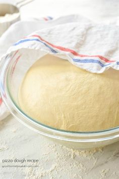 a pizza dough in a glass bowl on top of a white tablecloth with a red, white and blue striped towel