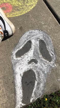 someone's feet standing on the sidewalk next to a chalk drawing of a face