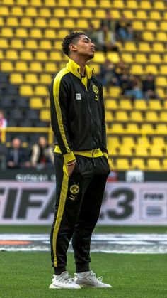 a man standing on top of a soccer field wearing black and yellow tracksuits