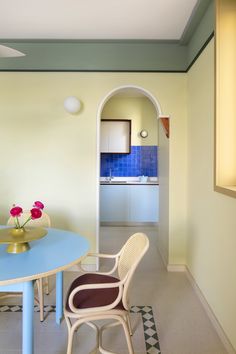 a blue table and chairs in a room with yellow walls, checkered flooring and an archway leading to the kitchen