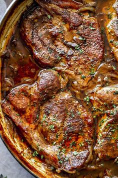 some meat is cooking in a pan with sauce and herbs on the side, ready to be eaten