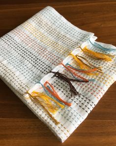 four different colored tassels are on a white cloth with yellow, orange, and blue thread