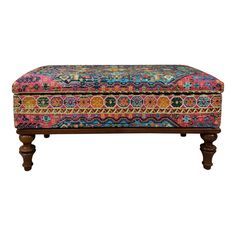 a colorful ottoman with wooden legs and an ornate pattern on the top, sitting in front of