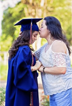 two women in graduation gowns are kissing each other