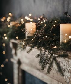 some candles are sitting on a mantle decorated with greenery and pine cones, surrounded by lights