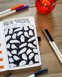 an open notebook with halloween images on it next to markers, pens and pencils