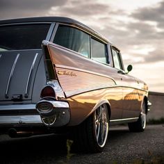 an old car is parked on the side of the road with clouds in the background