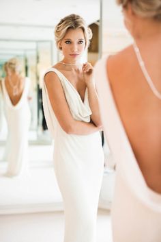 a woman in a white dress looking at herself in the mirror with her hand on her shoulder