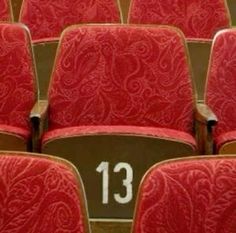 rows of red seats with numbers on them in an auditorium or theater setting, showing the number thirteen