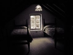 two beds in a dark room with an open window