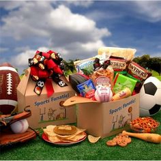 a football themed gift box filled with snacks and sports items sits on the grass in front of a blue cloudy sky