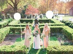 three bridesmaids standing in the middle of a garden with white balloons and greenery