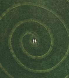 two people are standing in the middle of a circular grass field, looking down at each other